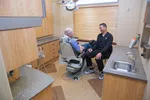 Dentist talking and smiling with elderly male patient seated in dental chair in modern clinic room.