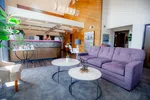 Bright modern lobby with purple sofa, marble coffee tables, wooden panel wall, and receptionist desk area.