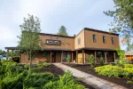 Modern brown two-story dental office building with surrounding greenery and clear sky background.