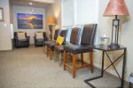 Well-lit waiting room with leather chairs, side tables, lamps, and a sunset landscape painting on the wall.