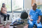 Dentist in blue scrubs talking to patient reclining in chair