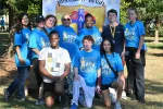 Group of diverse people wearing blue Race for a Cure shirts posing outdoors at a charity event.