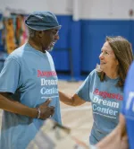 Two smiling adults wearing Augusta Dream Center shirts sharing a warm moment indoors at a community event.
