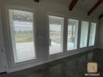 Row of tall white windows with horizontal blinds in a modern room with exposed wooden ceiling beams.