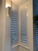 White plantation shutters cover corner windows in a modern, well-lit interior space with minimal decor.