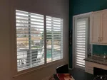 Kitchen interior with white plantation shutters on windows and door overlooking a backyard pool.