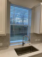 Modern kitchen sink with chrome faucet under window with white blinds and hexagonal tile backsplash.
