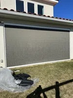 Gray exterior solar screen covering a large window on a modern house with beige walls and red roof tiles.