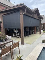 Outdoor covered patio with brown wood structure, black retractable shades, wooden furniture, and a poolside seating area.