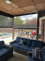 Covered outdoor patio with blue cushioned wicker furniture, ceiling fan, string lights, and view of backyard pool.