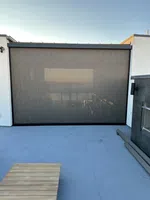 Modern outdoor patio with a large retractable screen, wooden bench, and minimalist concrete floor under clear sky.