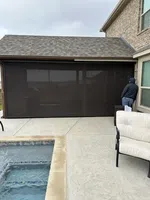 Covered patio with a mesh screen enclosure, pool edge, and patio furniture on a cloudy day.