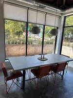 Modern dining room with concrete table, leather chairs, large windows, and pendant lights with outdoor view.
