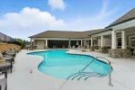 Outdoor swimming pool with lounge chairs, umbrellas, and covered patio under a partly cloudy sky.