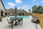 Modern outdoor pool area with black and white striped umbrellas, loungers, and seating under blue sky.