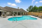 Outdoor residential swimming pool with lounge chairs, umbrellas, and a covered patio area on a sunny day.