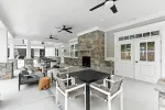Spacious covered patio with stone fireplace, modern dining table, lounge chairs, and ceiling fans in a bright setting