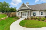 Modern suburban house with stone and siding exterior, white door, green lawn, and concrete walkway under blue sky.