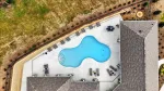 Aerial view of an irregularly shaped pool surrounded by lounge chairs and buildings in a landscaped outdoor area.