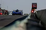 Blue Acura race car exiting pit lane during a motorsport event under clear sky.
