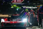 Acura race car in pit stop with crew refueling and changing tires during night race event.
