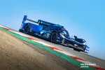 Blue and black Acura race car number 10 speeding on a curving racetrack under clear blue sky.
