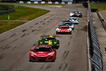 High-performance race cars compete closely on a paved track during a professional motorsport event.