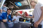 Racing drivers signing autographs and interacting with fans at a Konica Minolta event tent outdoors