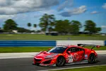 Red Acura NSX GT3 race car number 93 speeding on a racetrack with blurred background and blue sky.