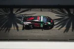 Black and red race car with number 45 speeding on a sunlit track casting palm tree shadows.