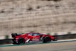 Red Lamborghini race car speeding on a desert racetrack with sponsor logos and racing decals.