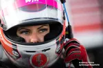 Close-up of a race car driver wearing a helmet and red gloves, preparing for the race with focused eyes.