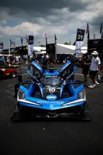 Blue Acura race car with doors open at motorsport event with people and tents in background under cloudy sky