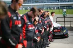 Racing team and driver standing in a line with a DEX black race car at pit lane marked 45.