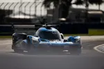 Blue and black LMP race car speeding on a sunlit racetrack with bright LED headlights.