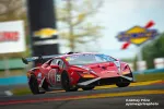 Red Lamborghini race car speeding on track with sponsor logos and blurred background during race event