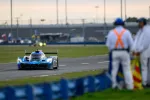 Blue Acura racing car on track with race officials watching during a motorsport event at dusk.