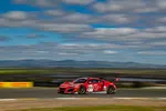 Red race car number 93 speeding on race track under blue cloudy sky with blurred background.