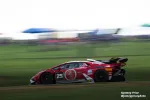 Red race car number 25 speeding on a racetrack with blurred background and grassy edges.