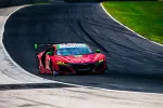 Red Acura race car with green accents speeding on a curving race track under sunny skies.