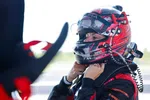 Race car driver adjusting helmet strap preparing for a race in full racing gear outdoors.