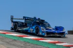Blue Acura racecar number 10 speeds over a turn on a race track with red, white, and green curbs under clear sky