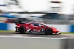 Red Lamborghini race car speeding on track with sponsors and racing decals in a professional motorsport event.