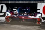 Red Acura race car number 40 with bright LED headlights speeding on a racetrack during a race.