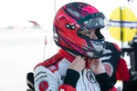 Race car driver adjusting red and black helmet with racing suit and Acura logo in pit area before race.