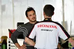 Two men in a garage area, one in a Honda HPD team shirt talking to a man in racing gear.