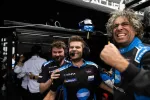Three Acura racing team members celebrating with headsets in the pit area showing excitement and victory.
