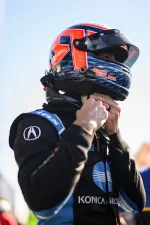 Race car driver in black and blue Konica Minolta suit fastening helmet strap before race.