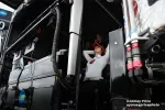 Race team members in white uniforms inside a black racing pit box with technical equipment and cables.