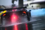 Black race car number 45 speeding on wet track with red taillights and water spray on rainy day.